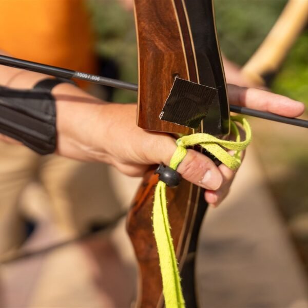 Main d'archer avec brassard et dragonne tenant un arc classique et une flèche
