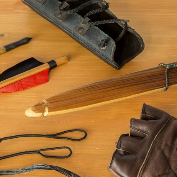 Matériel d'archer posé sur une table en bois : brassard en cuir, flèches, branche d'arc, gant et corde