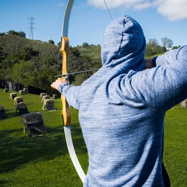 Archer vu de dos, bras tendus, bandant un arc face à un parcours de cibles en bottes de paille